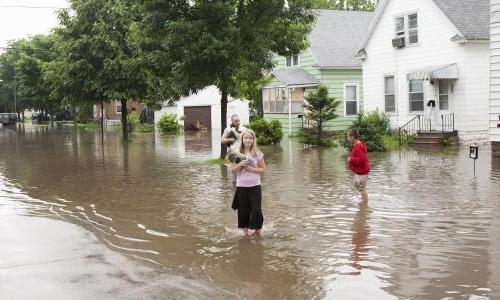 A family stands in ankle deep water holding some of their belongings. 